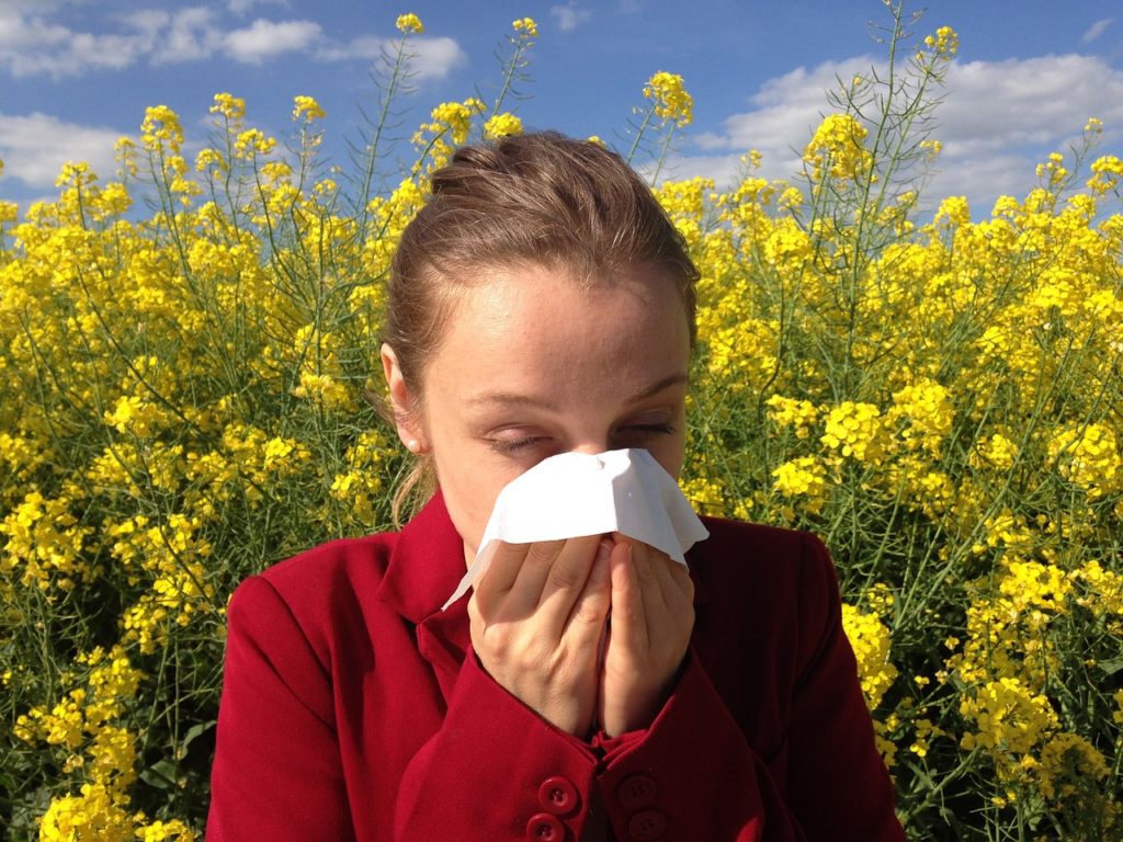 A woman blowing her nose into a tissue in front of yellow flowers